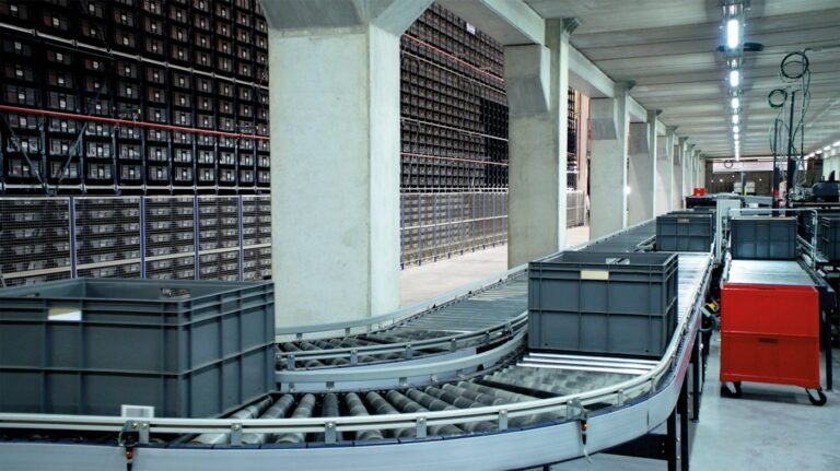 Roller conveyors carrying storage bins beside warehouse racks